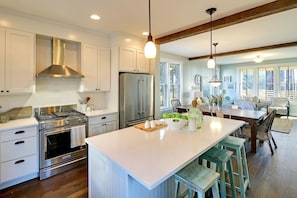 A modern kitchen with white cabinetry, stainless steel appliances, and a central island with stools.