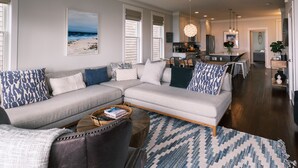 A modern living room with a sectional sofa, a coffee table, and a dining area with bar stools. - Seabrook Love Shack | Oceanfront, Hot Tub, Ocean Views, Sleeps 6 (Pacific Beach)