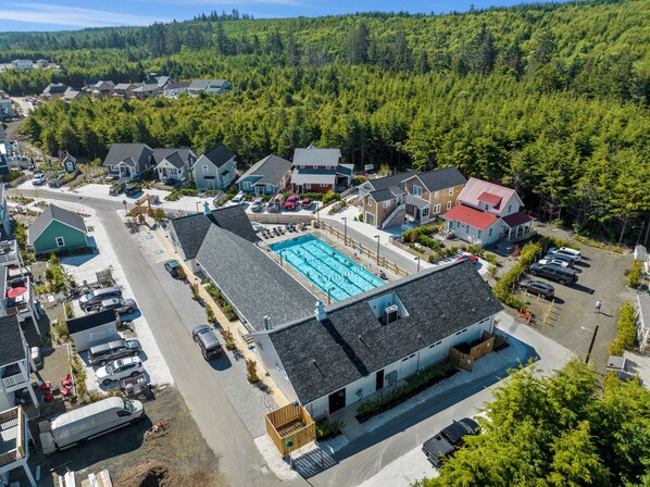 An aerial view of a residential area with a large swimming pool surrounded by houses, a road, and parked cars.
