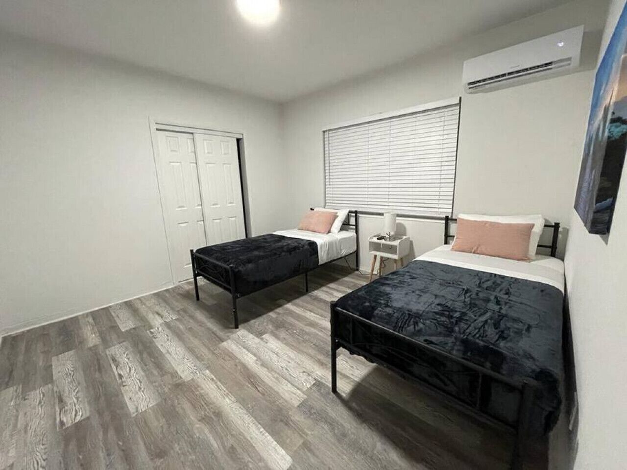 Quarto com duas camas, um guarda-roupa, uma mesa de cabeceira e uma janela com persianas.