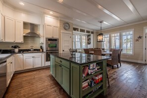 A spacious kitchen with white cabinetry, a green island, and a dining area with wicker chairs.