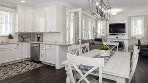 A modern kitchen with white cabinetry, a dining area with a white table and chairs, and a living room with a TV and seating. - Seabrook Northwest Passage | Hot Tub, Fire Pit 3BR | Sleeps 8, South of Market (Pacific Beach)