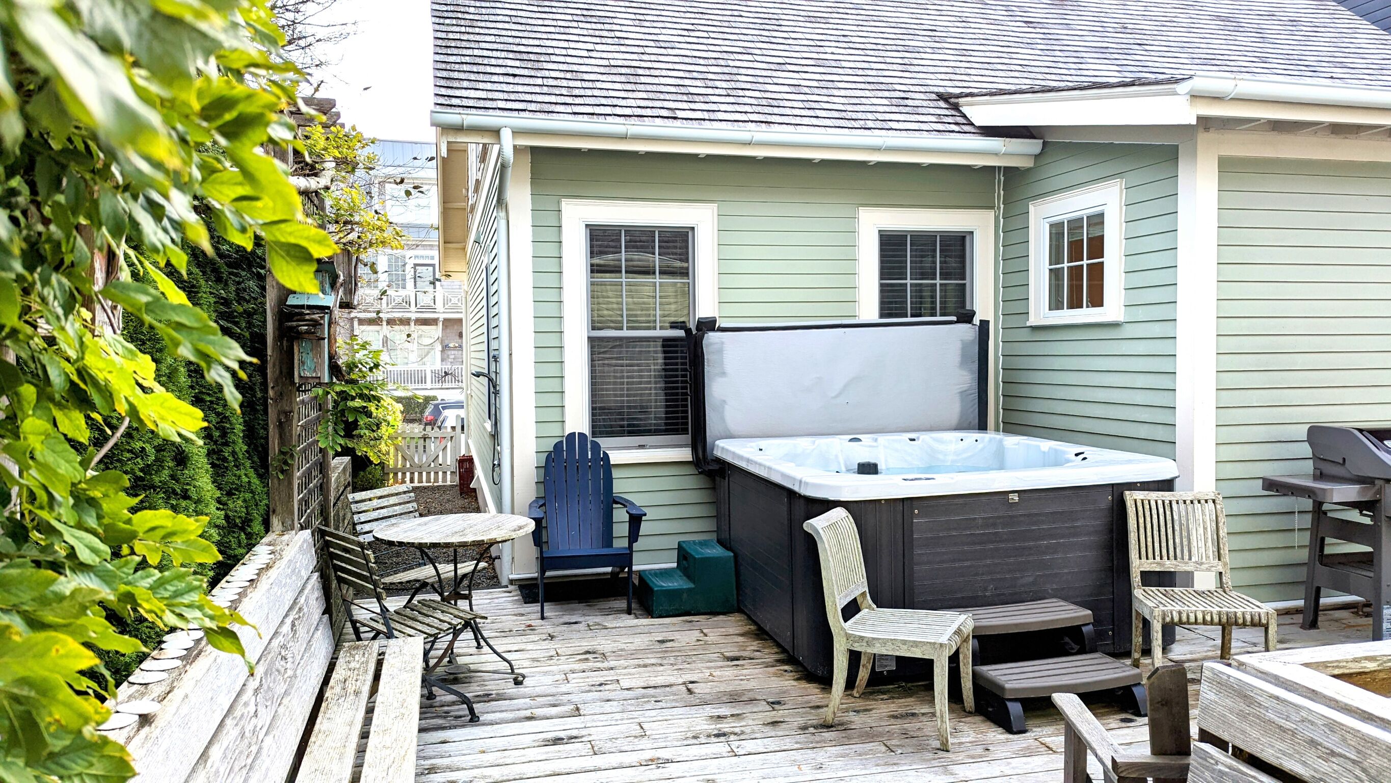 A patio with a hot tub, wooden chairs, and a table.