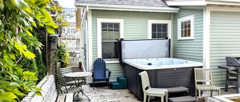 A patio with a hot tub, wooden chairs, and a table.