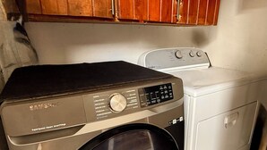 Een praktische wasruimte met een Samsung SuperSpeed Steam Smarthings wasmachine en droger, houten kasten erboven en een vloer van witte tegels.