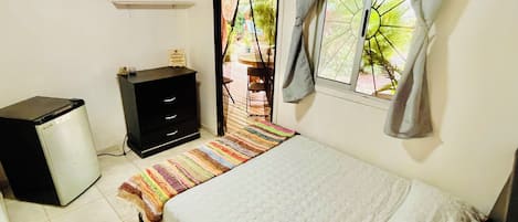 Een slaapkamer met een bed, een klein bureau, een stoel en een raam met gordijnen.