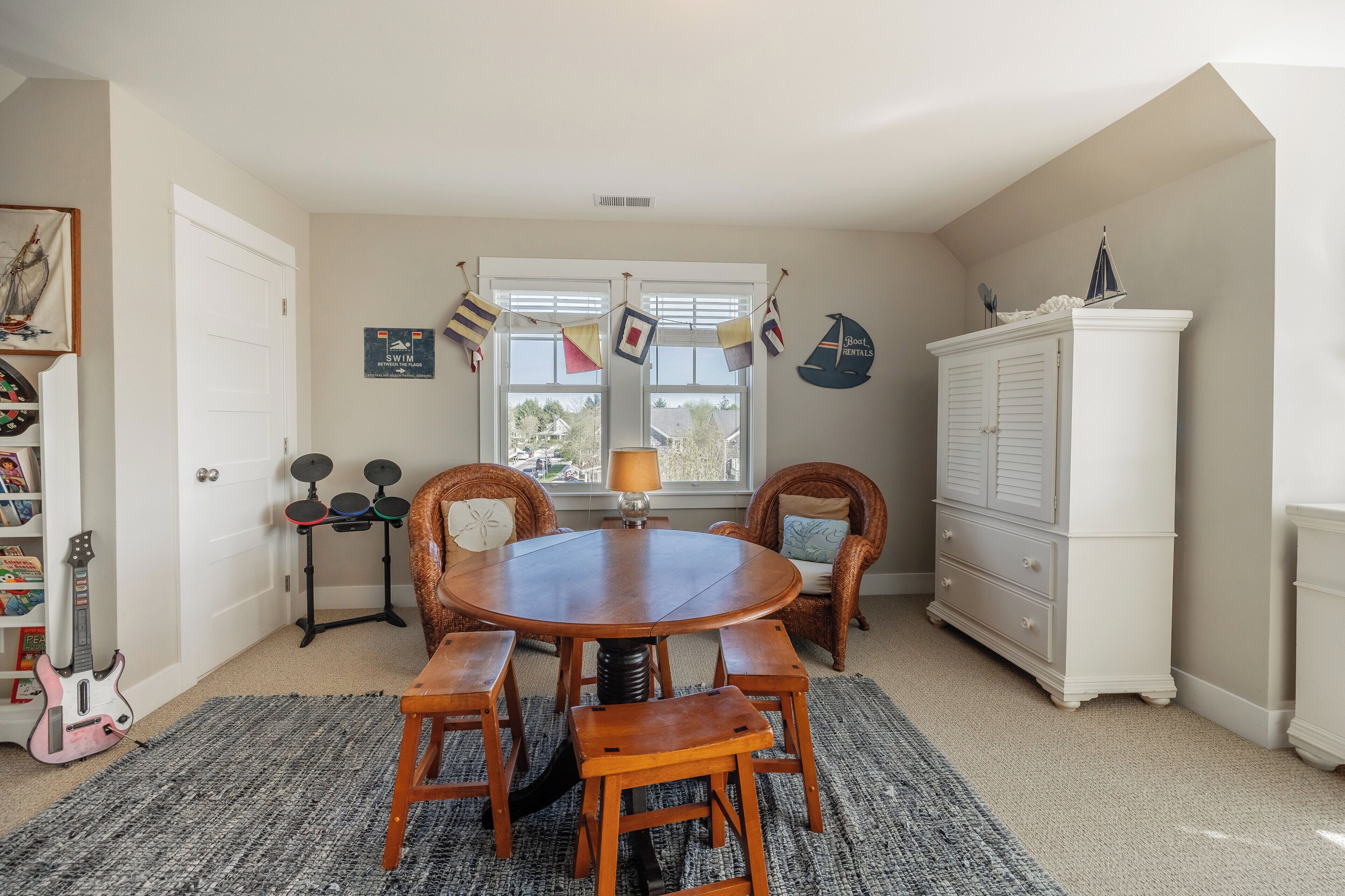 A dining area with a round wooden table and four chairs, a white cabinet, and a window with blinds.