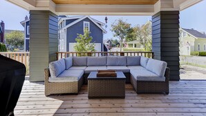 A covered outdoor seating area with a built-in sofa and coffee table, wooden deck flooring, and a view of neighboring houses. - *NEW* Seabrook's On The Rocks: Hot Tub & Dog Friendly (Pacific Beach)