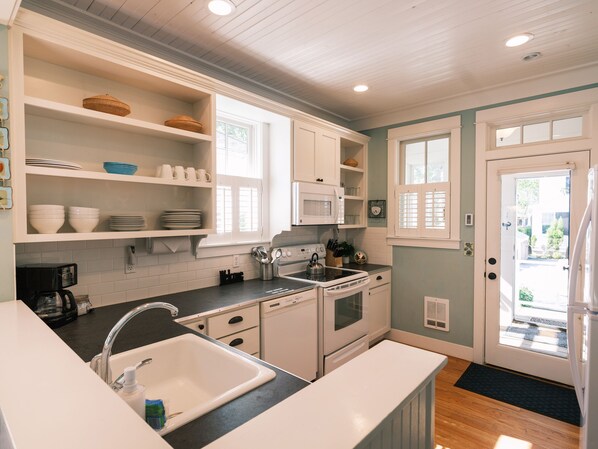 A kitchen with white cabinets, a stove, a microwave, and a sink. - Seabrook Periwinkle Cottage | Wood Stove, Park 2BR | Sleeps 5, North Alder (Pacific Beach)