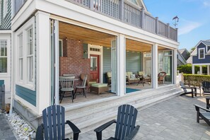 Une terrasse couverte, aménagée avec du mobilier d’extérieur, une cheminée en briques et une vue sur les maisons voisines.