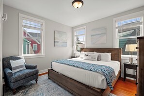 Une chambre à coucher avec un grand lit, une chaise, une table de chevet et une fenêtre donnant sur une maison.