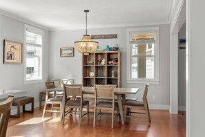 Un coin repas comprenant une table et des chaises en bois, un luminaire suspendu et une étagère décorative où sont exposés divers objets.