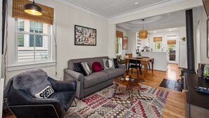 Ein Wohnzimmer mit Sofa, Sessel und Couchtisch, im Hintergrund eine Küche und ein Essbereich.
