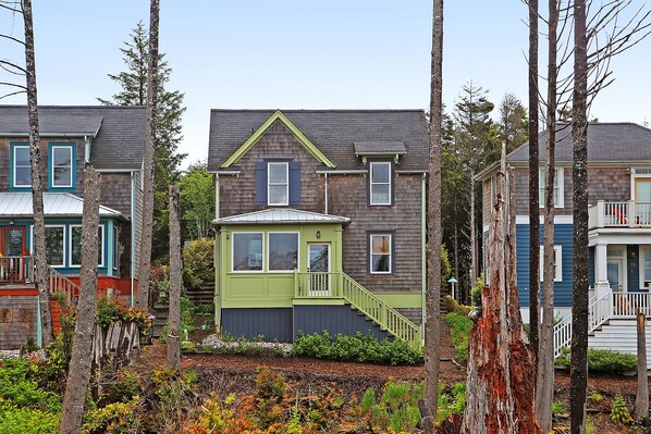 A row of two-story houses with a distinct green front house, surrounded by trees.