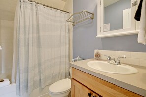 A bathroom with a shower curtain, a toilet, a sink with a mirror, and a towel rack.