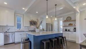 A modern kitchen with white cabinetry, a central island with stools, stainless steel appliances, and pendant lighting. - *NEW* Sand by Me, a beautifully furnished farmhouse! (Pacific Beach)