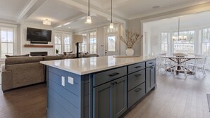 A spacious kitchen with a large island, dark blue cabinetry, and a dining area with a white table and chairs. - *NEW* Sand by Me, a beautifully furnished farmhouse! (Pacific Beach)