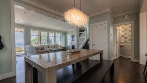 A spacious living area with a large wooden table, a sofa, and a staircase leading to an upper level. - Seabrook Sandy Side Up | Oceanfront, Hot Tub | 4BR, Sleeps 10, Seastack Views (Pacific Beach)