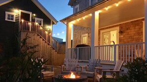 Une terrasse extérieure couverte, dotée d’un foyer, de chaises en bois et de guirlandes lumineuses.