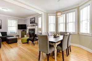 A dining area with a wooden table and patterned chairs, a fireplace, and large windows. - *NEW* Seabrook's Seas the Day: Dog Friendly! (Pacific Beach)