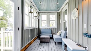 A covered porch with a blue bench, a small table, and a clock on the wall.