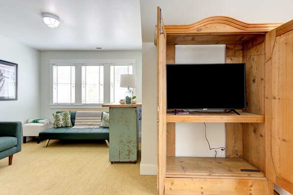 A living room with a green sofa, a small table with a lamp, and a wooden TV stand with a flat-screen TV.