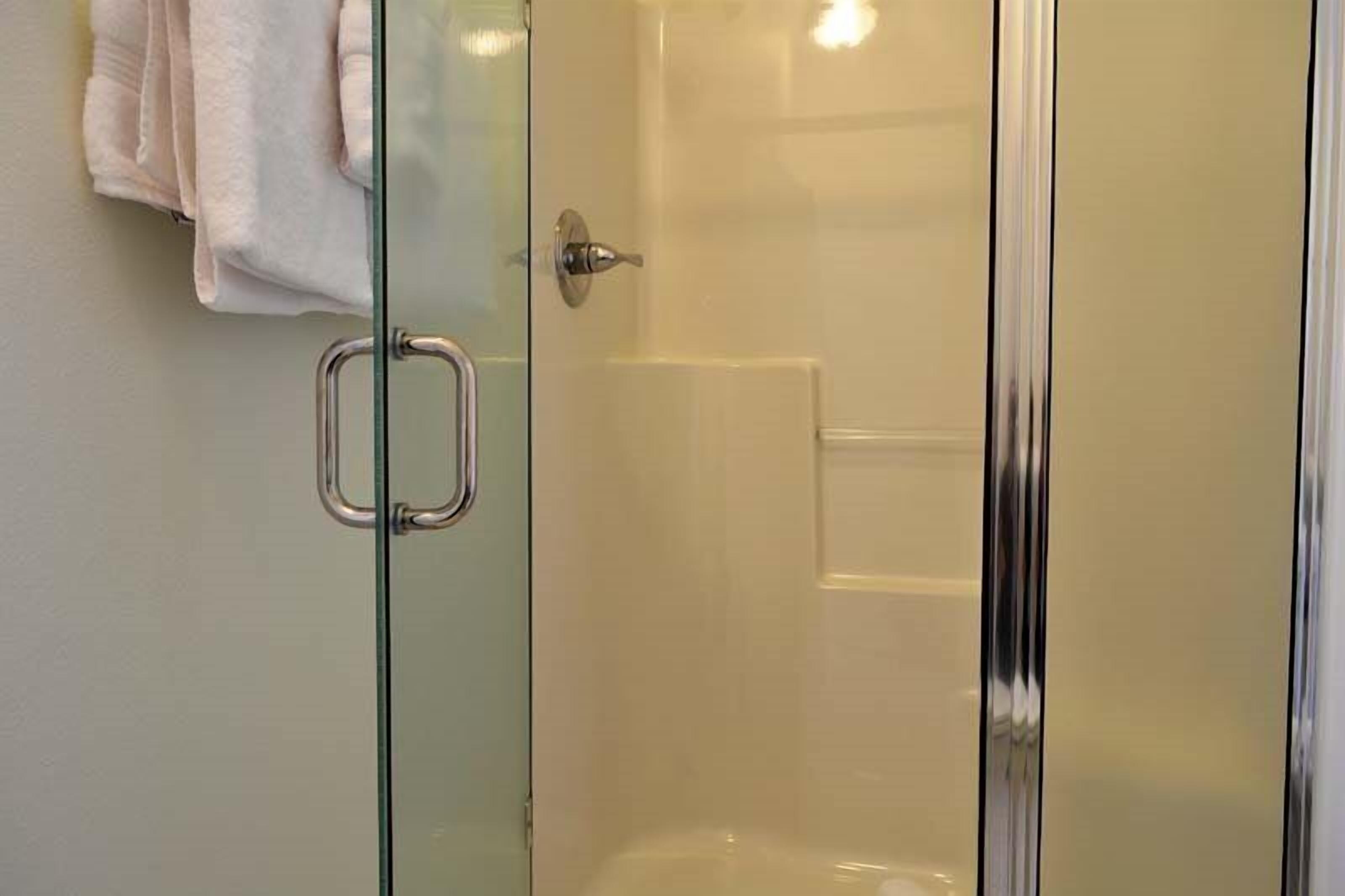 A glass-enclosed shower with a metal handle and a towel rack with a folded towel.