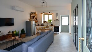 Een moderne keuken met een inbouwoven, een eethoek met een lange tafel en stoelen, en een grote grijze bank in de woonkamer.