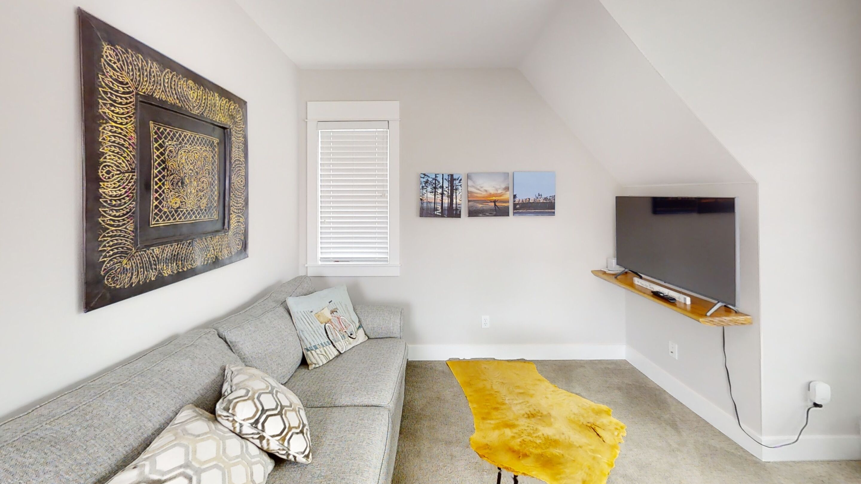 A modern living room with a grey sofa, decorative pillows, a large framed artwork, a yellow rug, and a mounted TV.