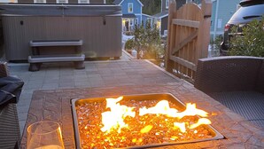 En terrasse med bålsted, siddepladser og udsigt til huse i baggrunden.