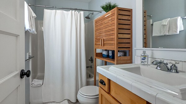 A bathroom with a shower curtain, a toilet, a sink with a mirror, and a wooden cabinet with shelves.