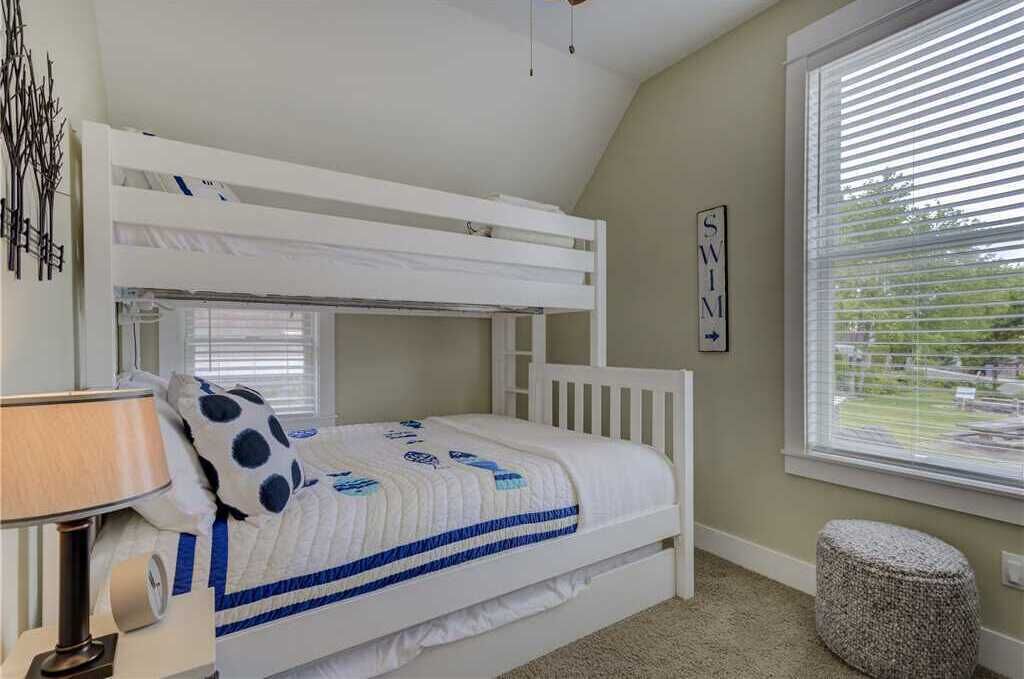 Une chambre avec un lit superposé, une fenêtre, une lampe et un petit tabouret.