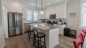 A modern kitchen with white cabinetry, stainless steel appliances, and a central island with bar stools. - Seabrook Somewhere in Time | Themed Rooms, Hot Tub | 4BR, Sleeps 11, South Farm (Pacific Beach)