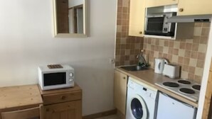 A compact kitchen with a microwave, washing machine, and stove. - Ski in/out Studio, sleeps 2/3 (Courchevel)