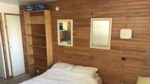 A bedroom with a wooden headboard, a bed with white bedding, a small bedside table with a lamp, and a mirror on the wall. - Ski in/out Studio, sleeps 2/3 (Courchevel)