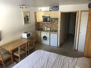A compact room with a bed, a small wooden table, a washing machine, a microwave, and a kitchenette. - Ski in/out Studio, sleeps 2/3 (Courchevel)
