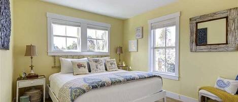 A bedroom with a bed, two bedside tables, a window, and a mirror.