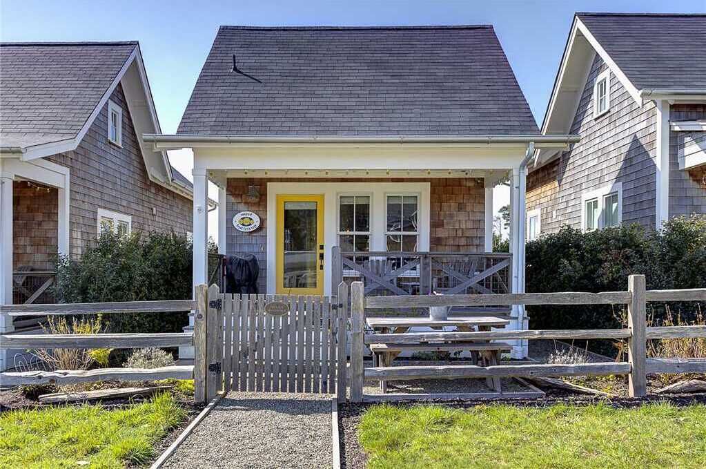 A two-story wooden house with a porch, a yellow door, and a wooden fence.