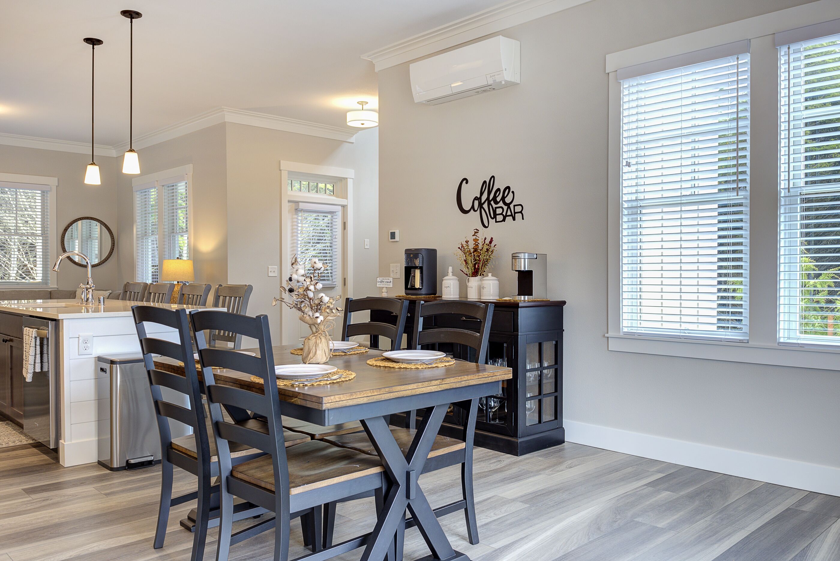 A modern kitchen with a dining area, featuring a coffee bar sign, built-in appliances, and a large window with blinds.