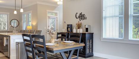 A modern kitchen with a dining area, featuring a coffee bar sign, built-in appliances, and a large window with blinds.