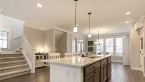 Une cuisine spacieuse dotée d’un îlot central, de luminaires suspendus et d’un escalier menant à un autre niveau.