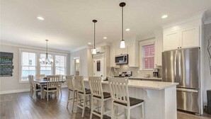 Une cuisine moderne avec des meubles blancs, des appareils en acier inoxydable et des luminaires suspendus.