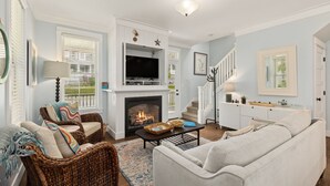 Una sala de estar con chimenea, televisor, muebles de mimbre y una escalera.