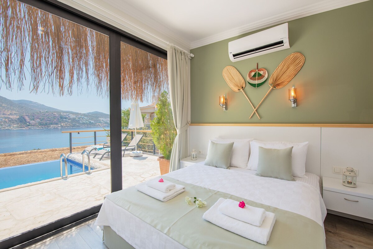 A hotel room with a bed, a view of a pool and water, and a wall-mounted air conditioner.
