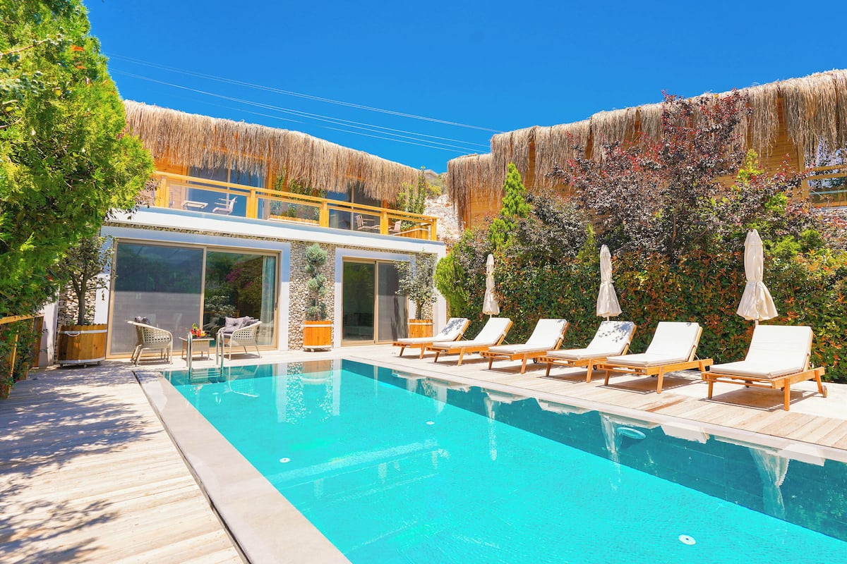 A swimming pool with lounge chairs and a building with a thatched roof.