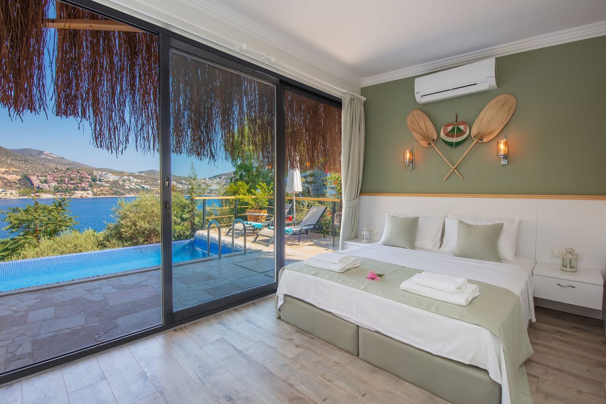 A bedroom with a large sliding glass door leading to a balcony with a pool and a view of a coastal landscape.