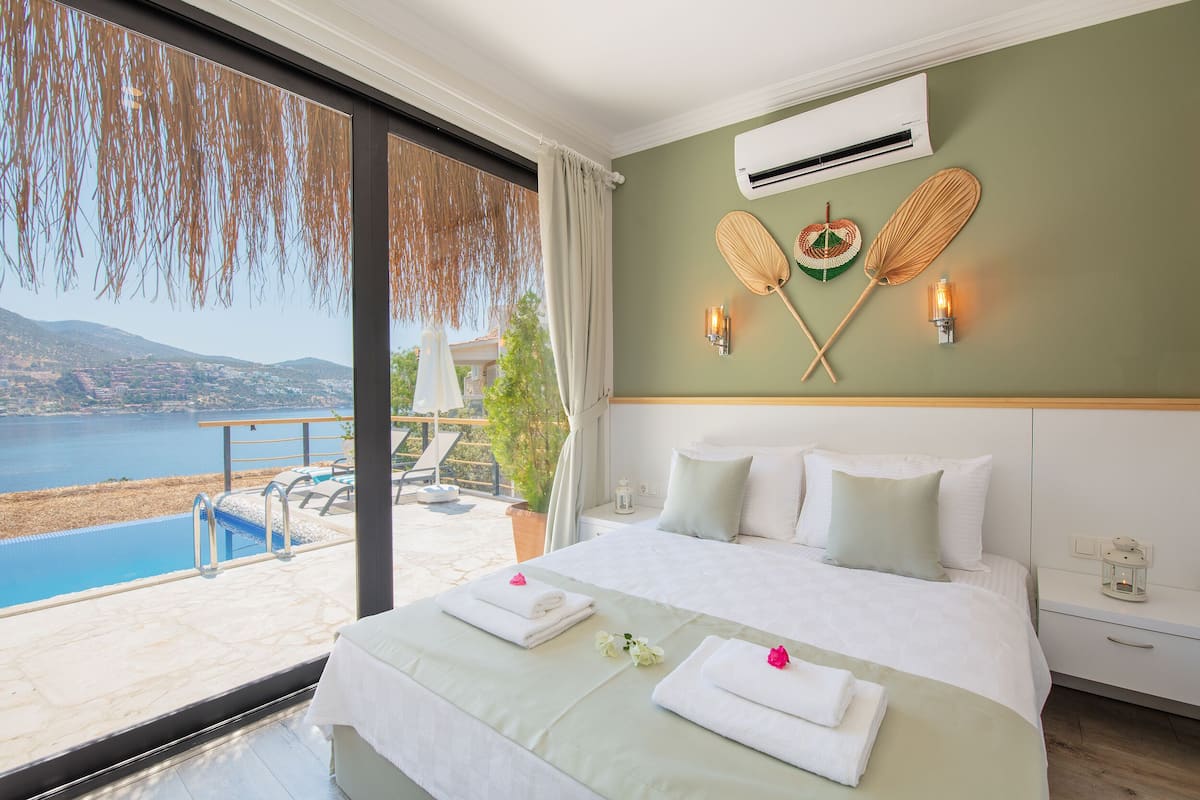 A hotel room with a bed, a view of a pool and water, and a wall-mounted air conditioner.