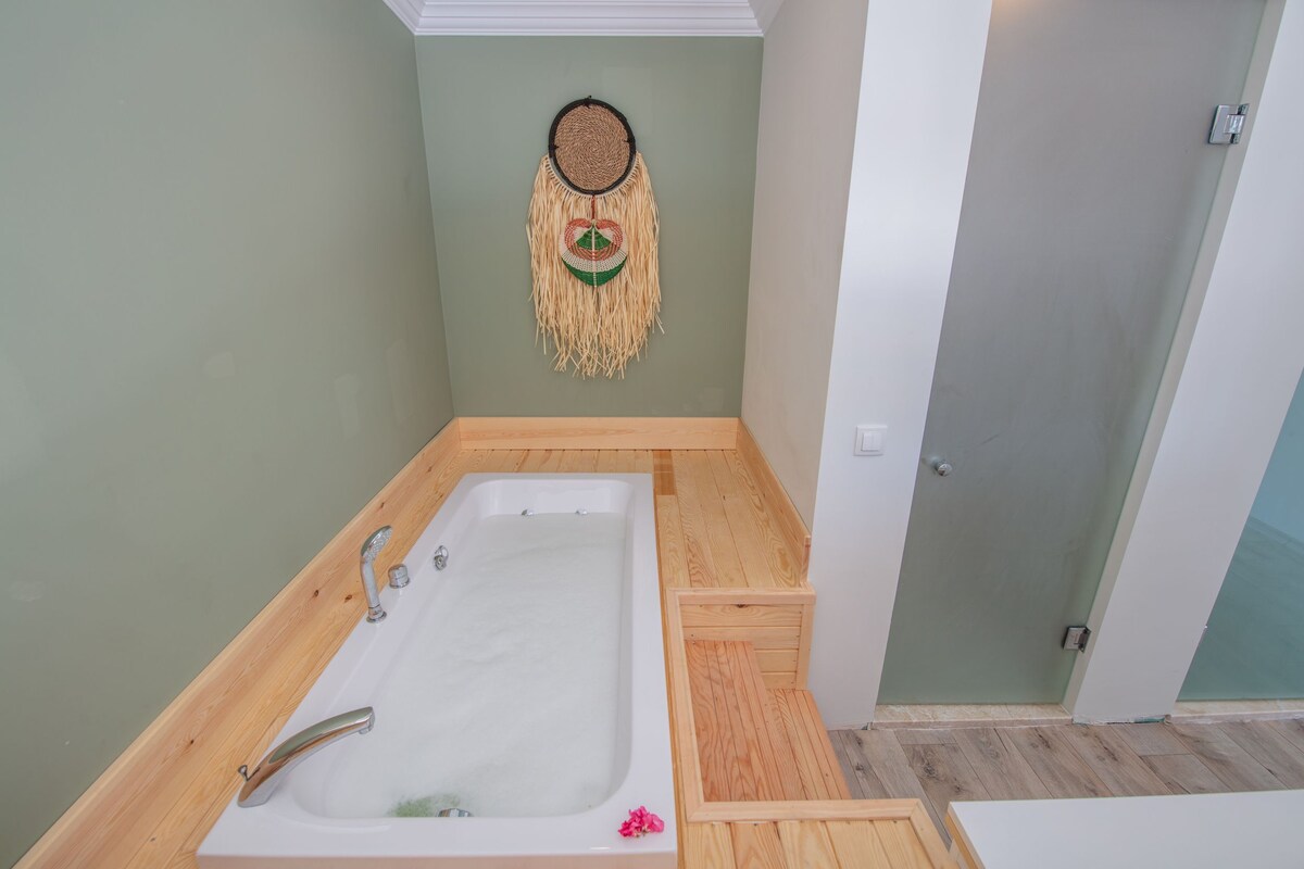A bathroom with a wooden bathtub, a wall-mounted dreamcatcher, and a door.