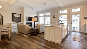 A spacious kitchen with a large island, a dining area with a wooden table and chairs, and a cozy seating area with a sofa and a lamp. - Seabrook The Penthouse | Ocean View, Pet Friendly | 1BR, Sleeps 4, Rooftop BBQ (Pacific Beach)