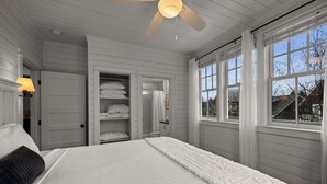 A bedroom with a large bed, white walls, a ceiling fan, and a window with curtains. - Seabrook Washington House | Piano, Sleeps 16+, 7BR | Historic Design, Crescent P (Pacific Beach)